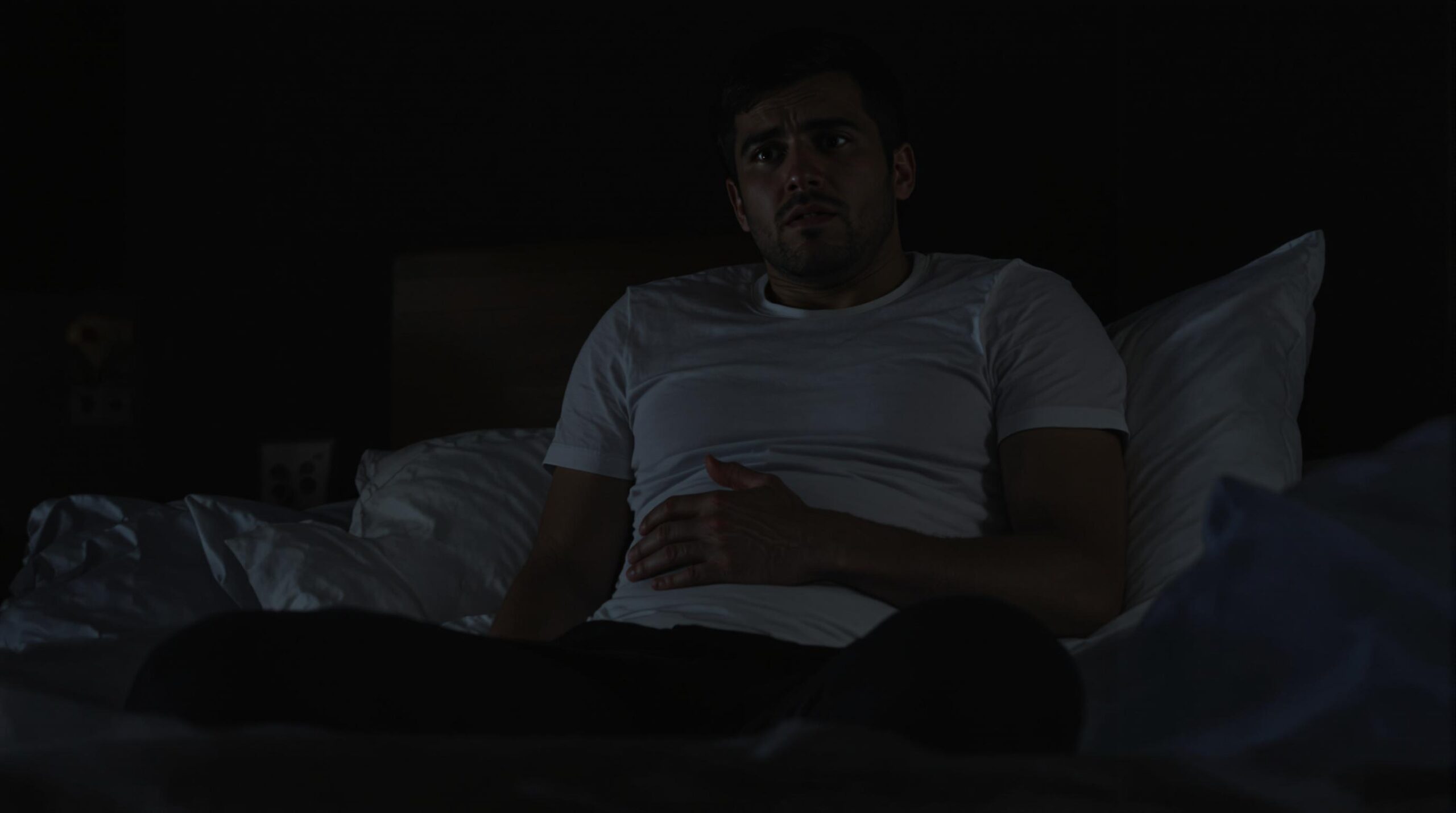 Man awake in bed with stomach pain at night
