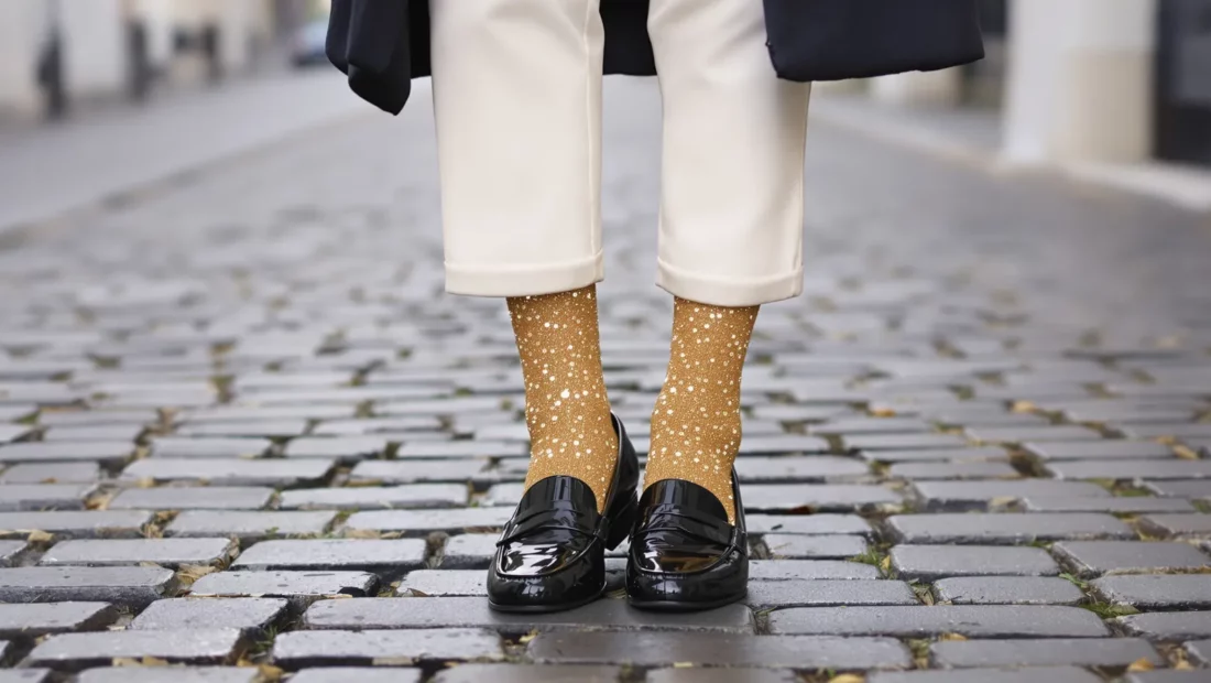 Chaussettes à paillettes dorées portées avec des mocassins vernis noirs et un pantalon écru