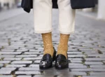 Chaussettes à paillettes dorées portées avec des mocassins vernis noirs et un pantalon écru