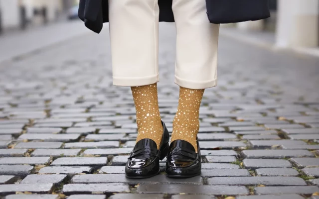 Chaussettes à paillettes dorées portées avec des mocassins vernis noirs et un pantalon écru
